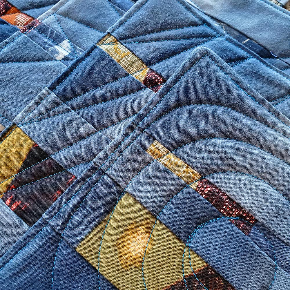 Photo of several small patchwork quilts stacked on top of eachother. They're made with faded blue fabric, with other fabrics in yellow and brown.