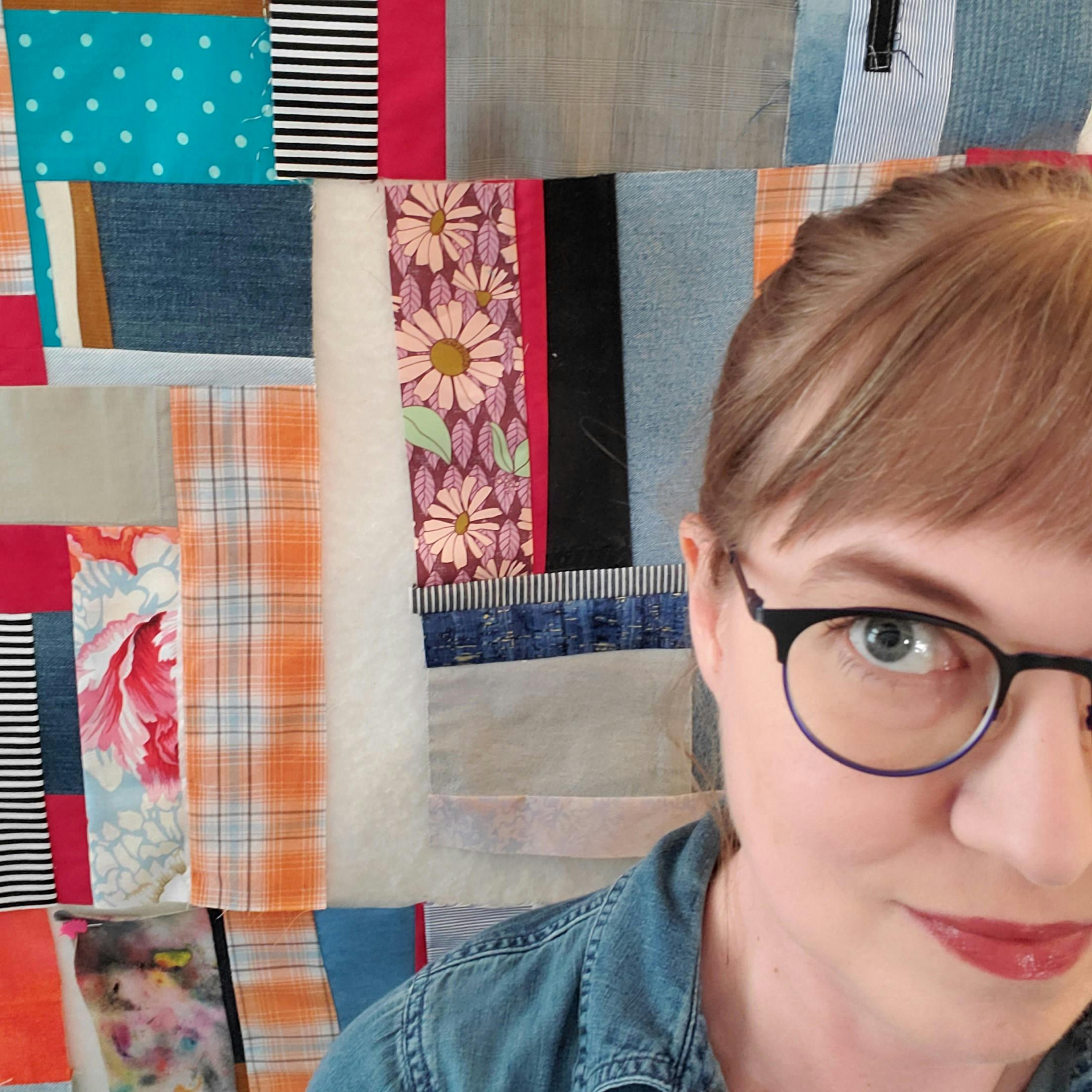 Selfie of Sarah sitting in front of her design wall with a patchwork quilt in progress.