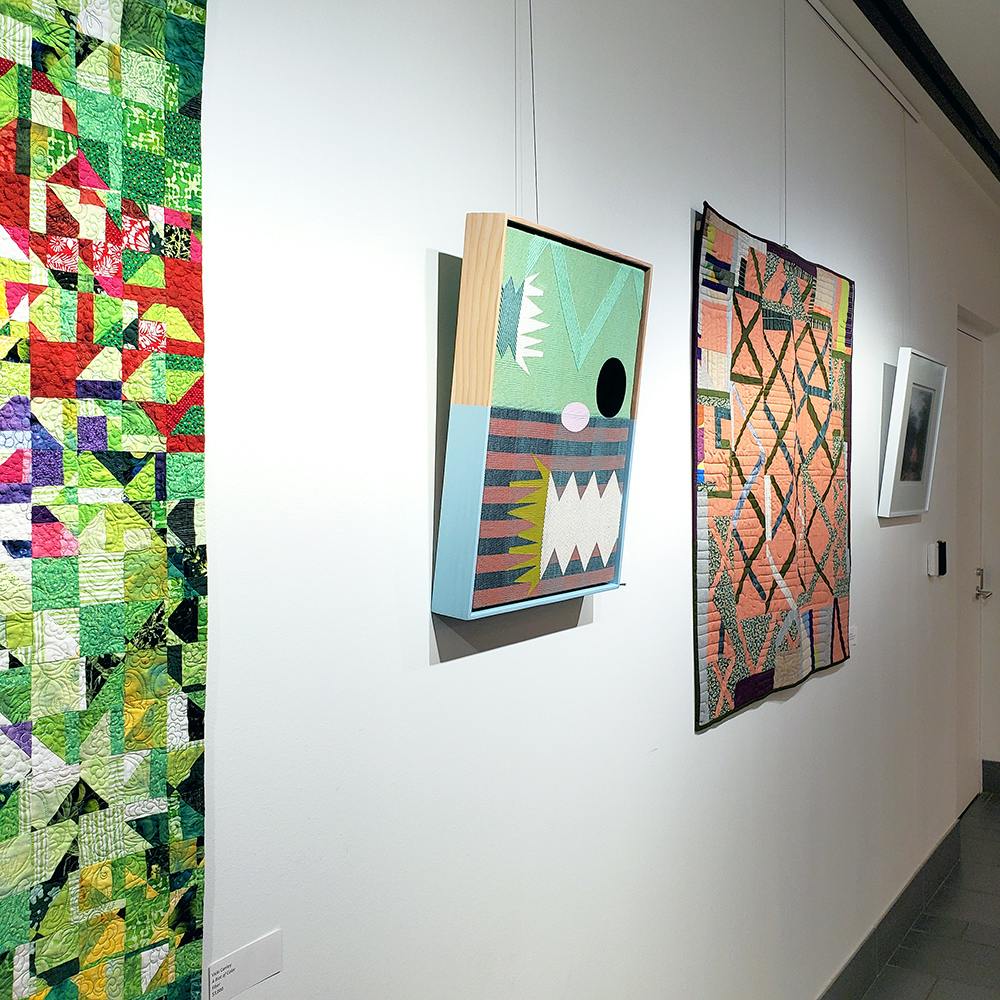 Photo of several fiber art works displayed on a gallery wall.