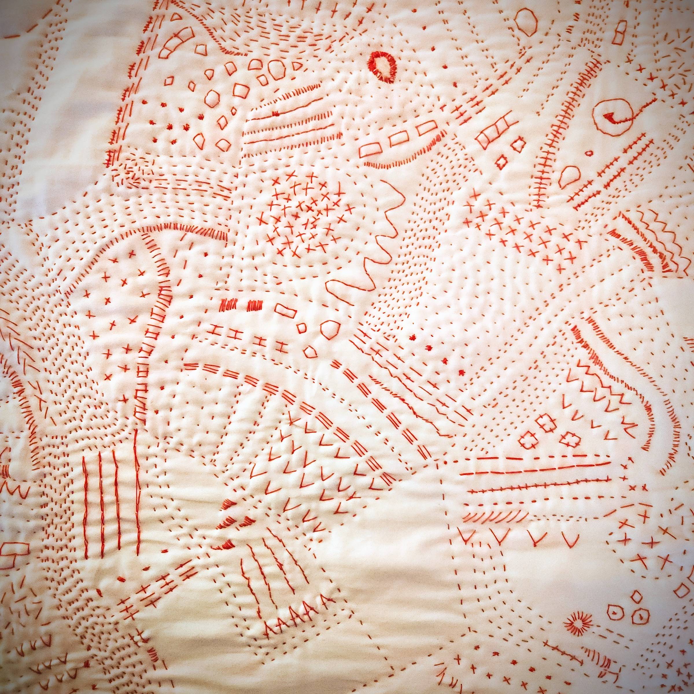 Digitally enhanced photo of a while pillowcase with red stitching all over. There are dots, lines, Vs, Xs, and other repetetive stitches.