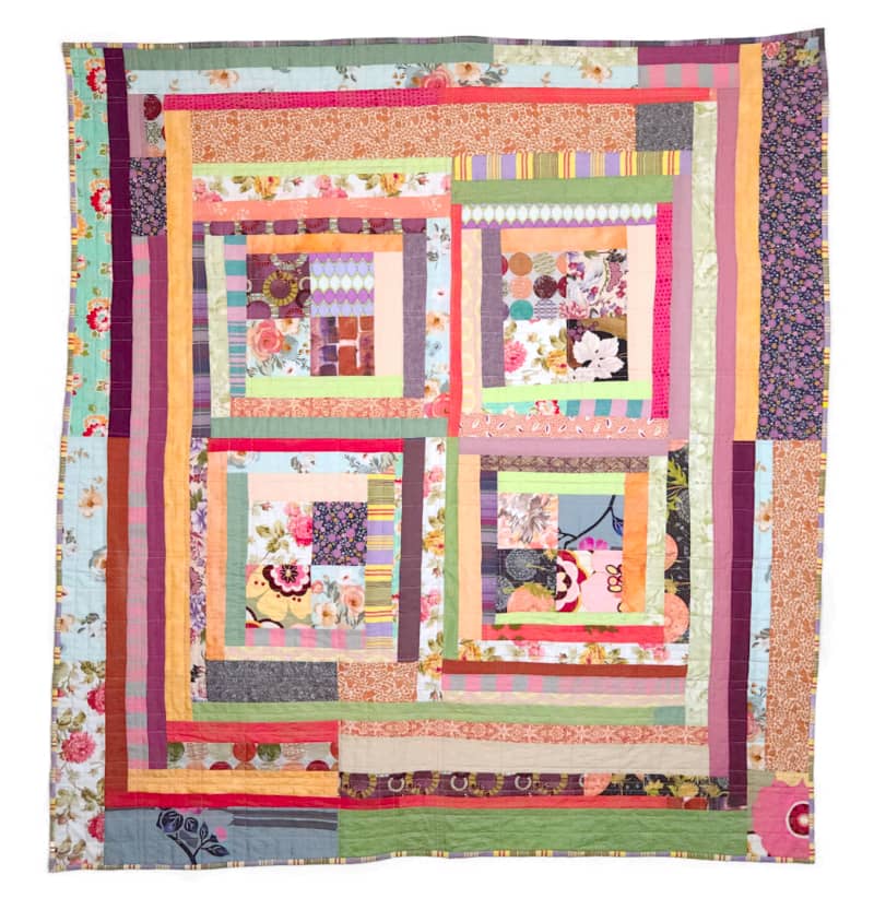 An improvised patchwork quilt, titled Boho Baby, created by Sarah Atlee. The overall design is squares surrounded by strips. The fabric colors are mainly pink, purple, orange, and pale green.