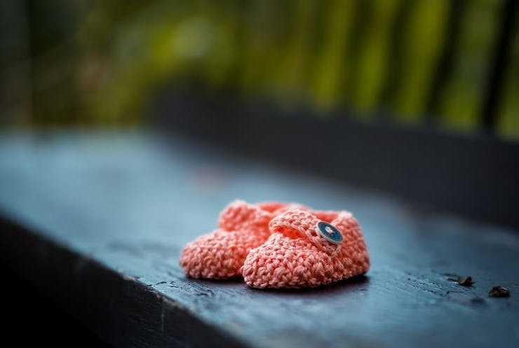 pair of baby's pink knit shoes on bench