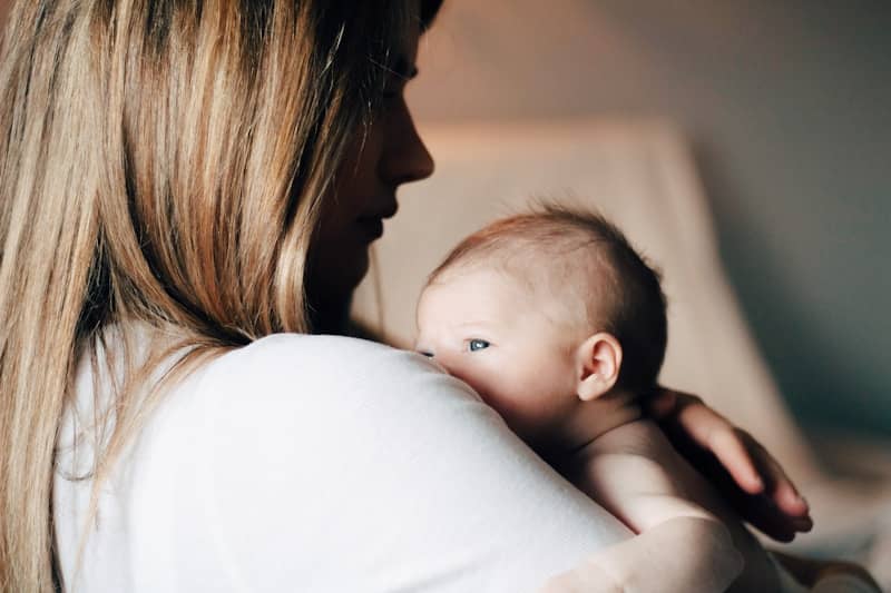 A mom, seen from the side, her face in the shadows, keeps a newborn close to her heart.