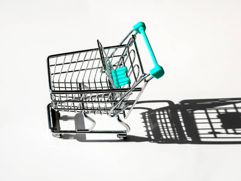 Small shopping cart with teal handles casting a shadow.
