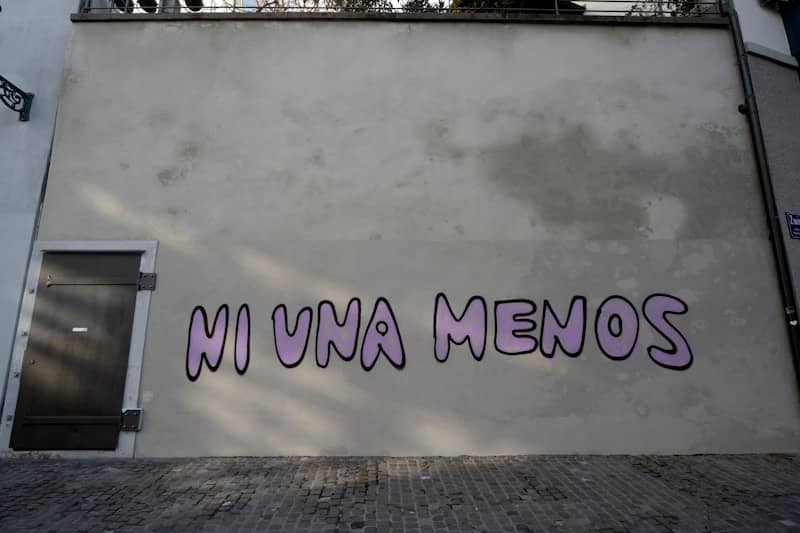 Purple "ni una menos" graffiti on a building wall.