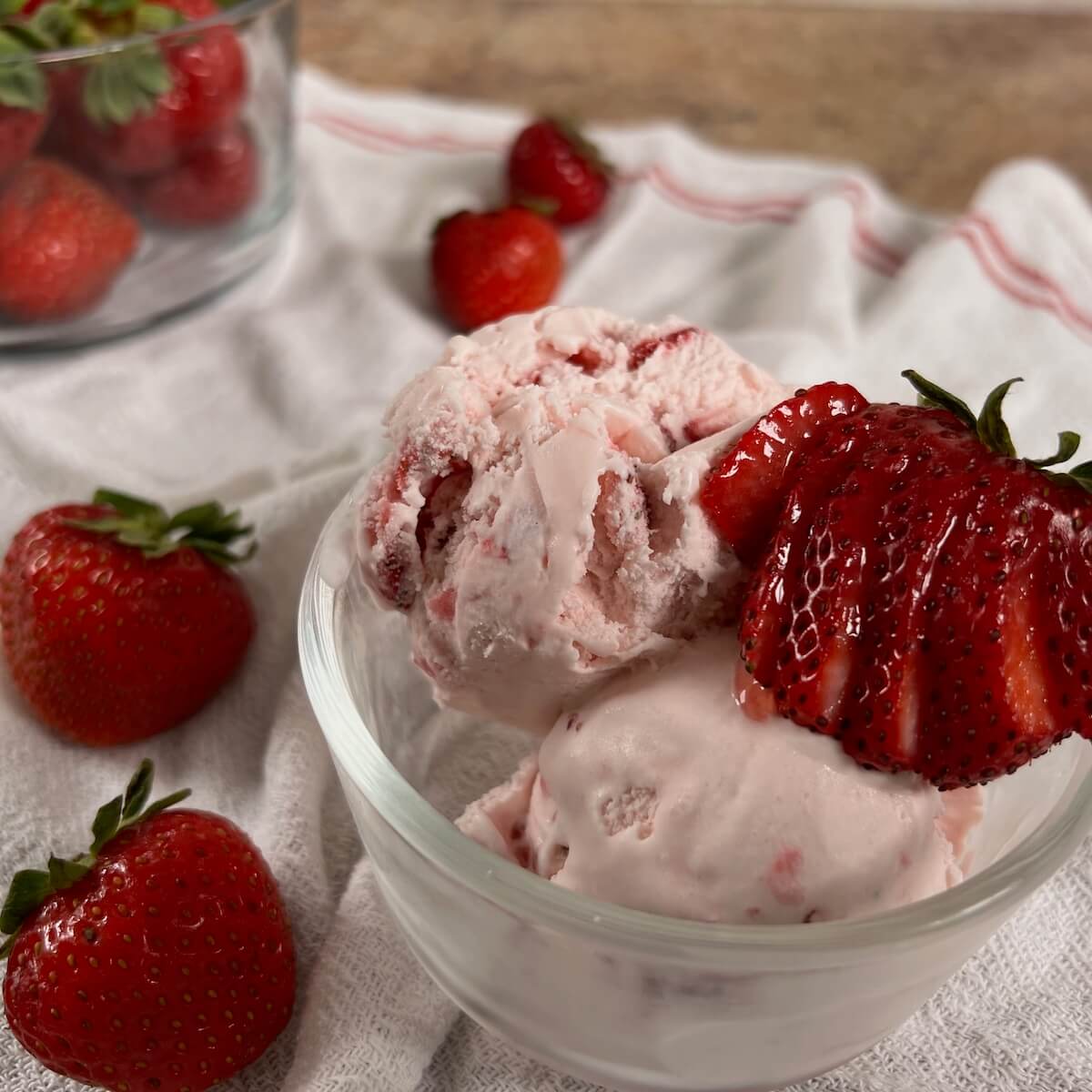 A bowl of strawberry ice cream with strawberries in a glass bowl.