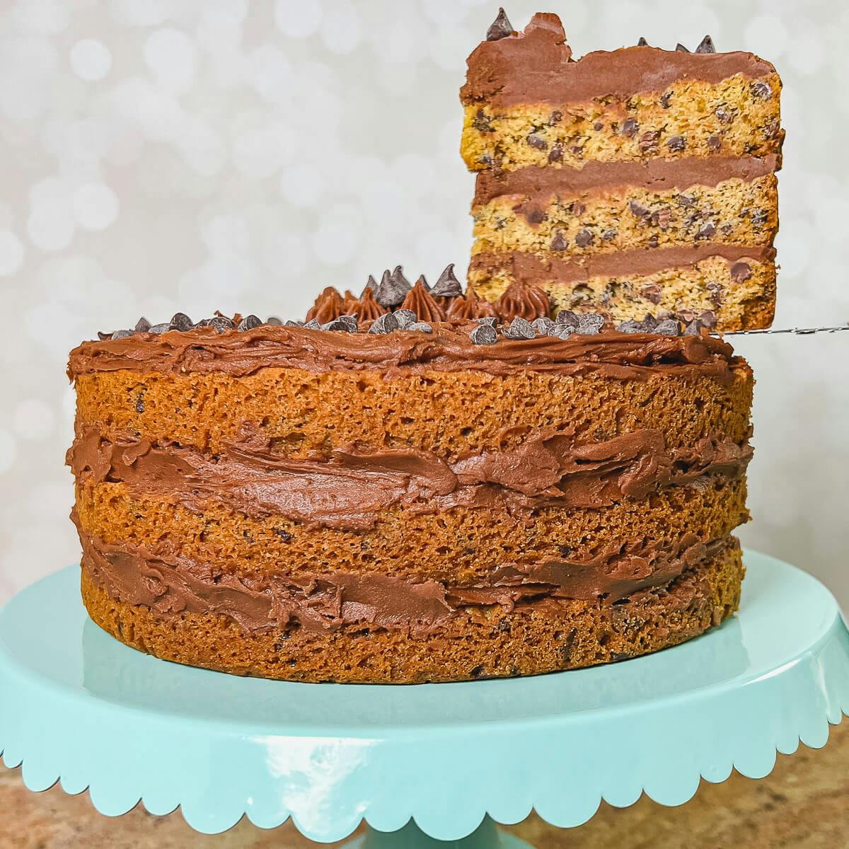 Whole Chocolate Chip Cookie Cake on a blue cake stand with a slice lifted.