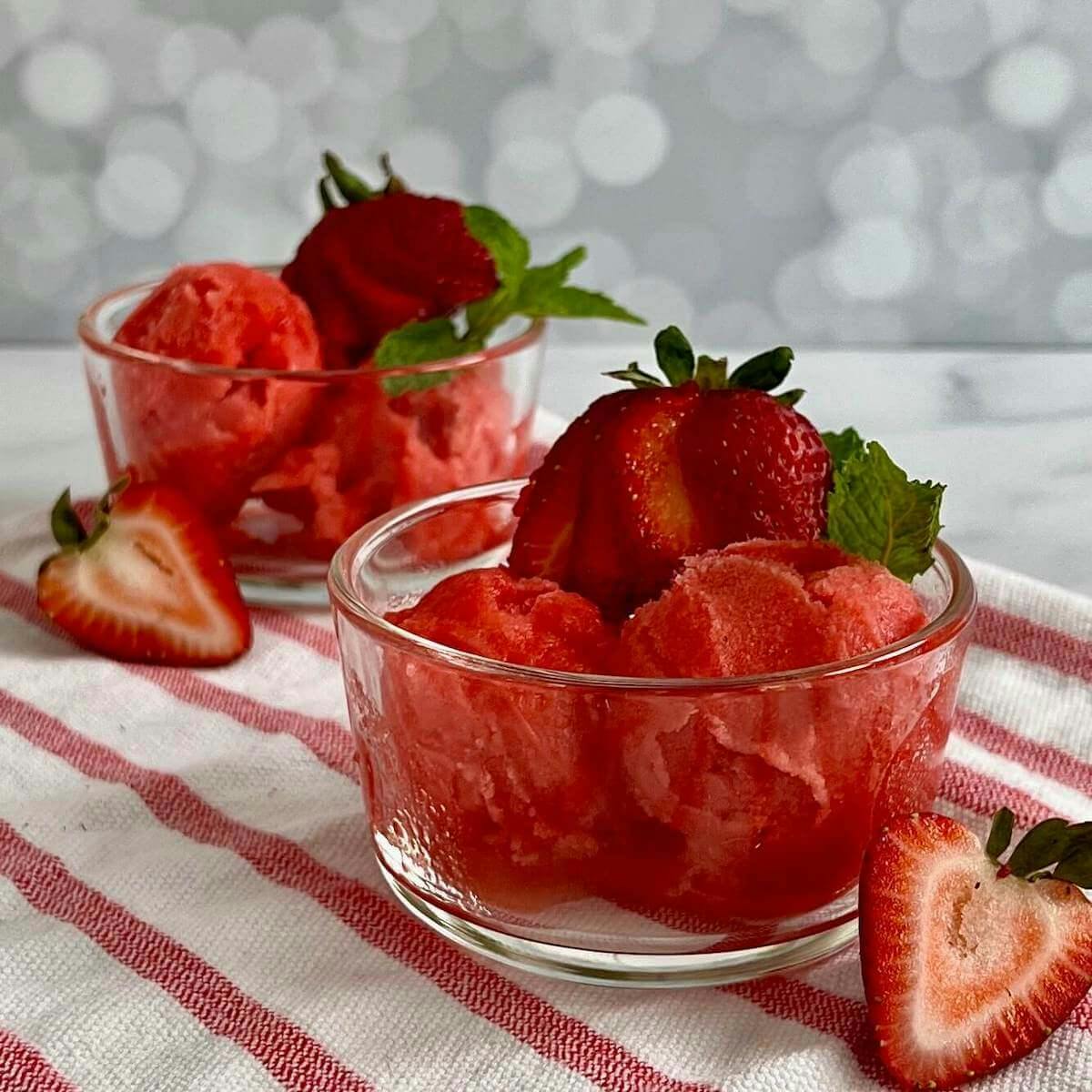 Two bowls of strawberry mint sorbet garnished with strawberries & mint on a red & white striped towel.