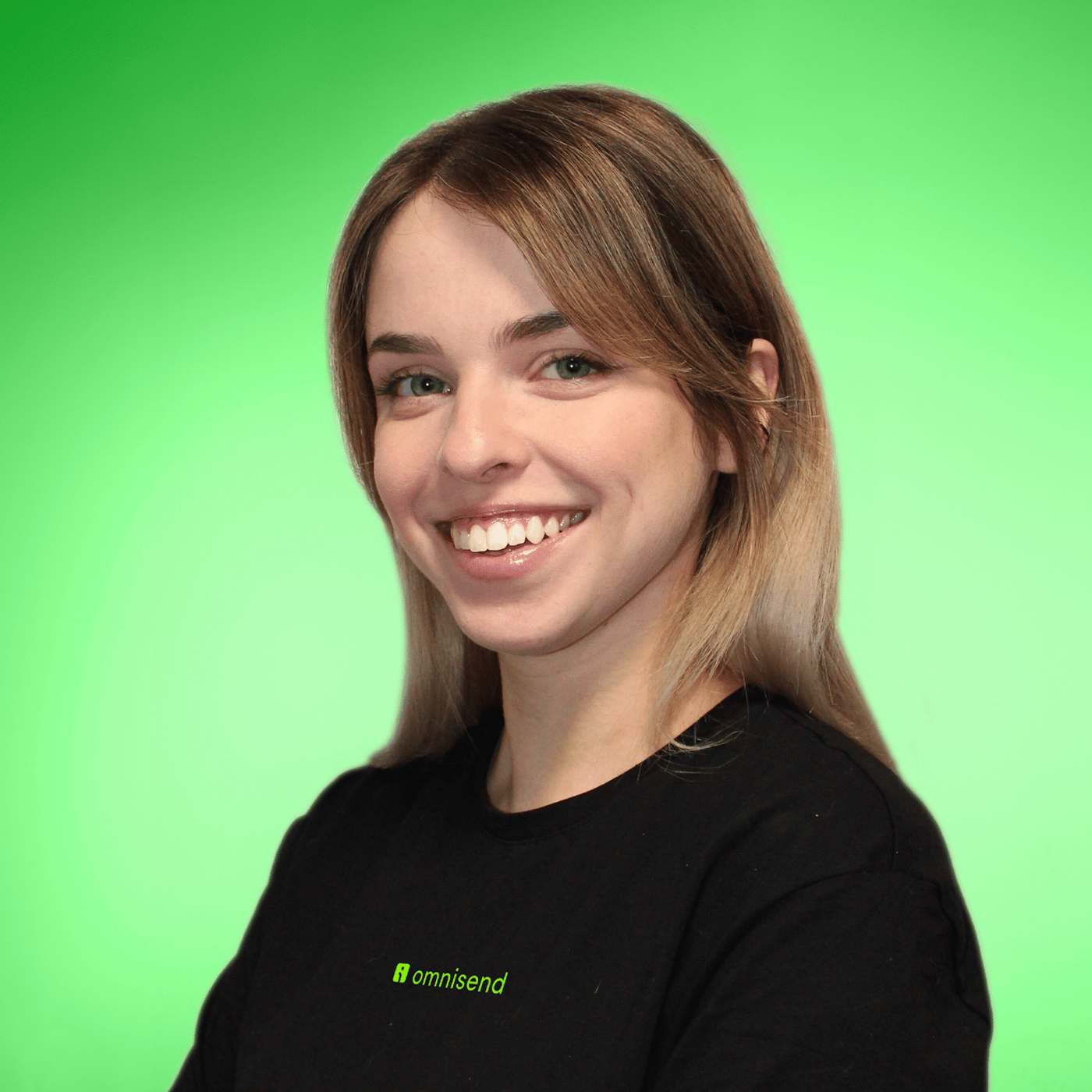 Ieva is a young woman with long brown hair, green eyes, and a bright smile. She is wearing a black t-shirt that says Omnisend. The background is gradient green.