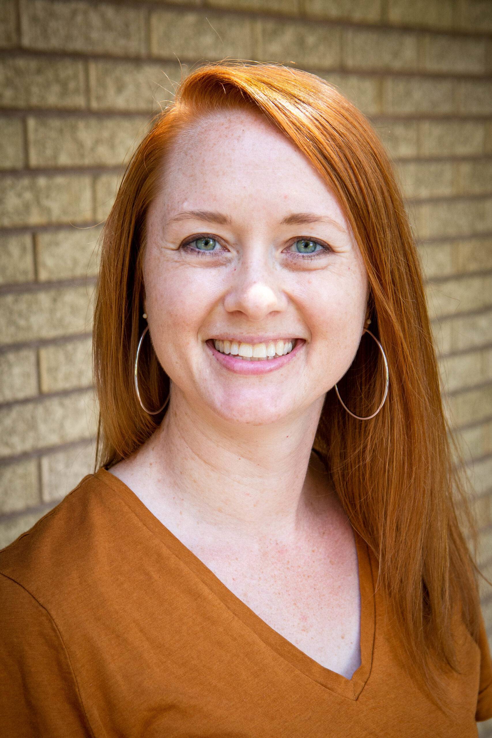 Headshot of Katie Richards with a beige brick wall in the background.