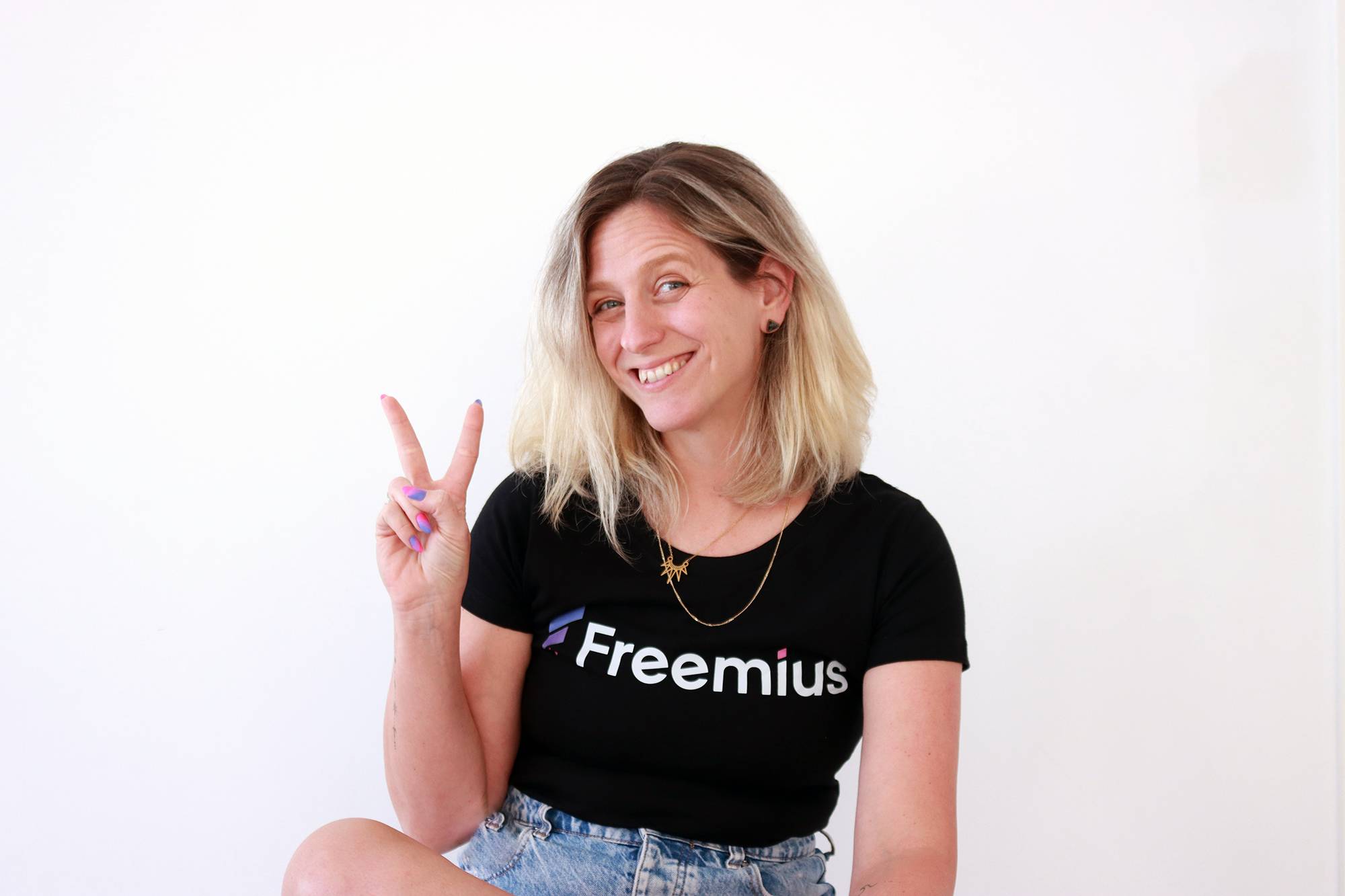 Hadas Golzaker, A woman wearing a Freemius t-shirt shows a peace sign with two fingers, smiling cheerfully.
