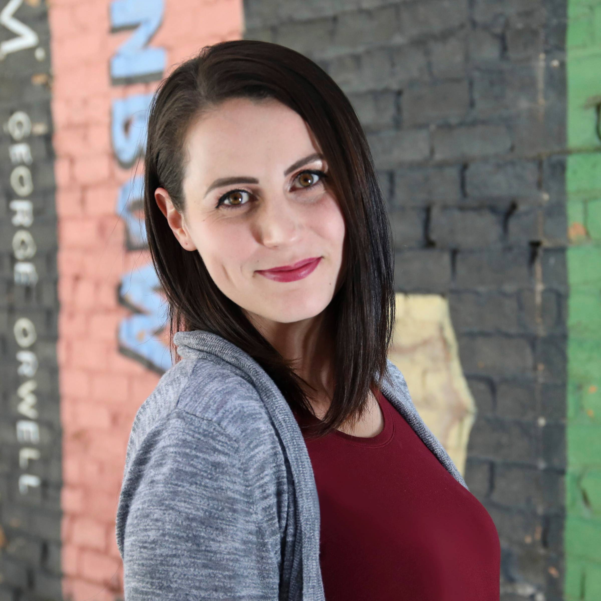 Jocelyn Hendrickson looking to camera with a colorful brick wall in the background