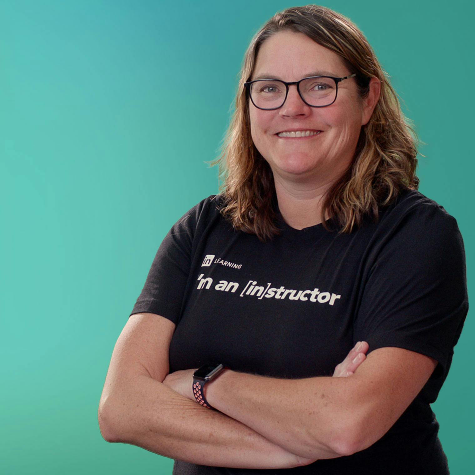 Carrie Dills in a  black t-shirt, arms crossed, with a green background