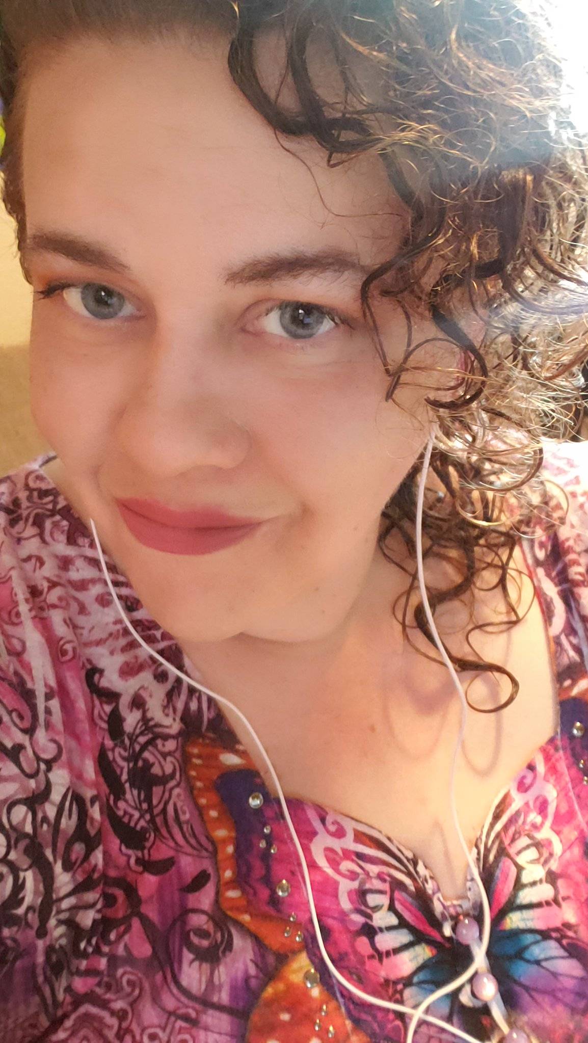 Headshot of Tia Wood. She has brown curly hair and is wearing a pink shirt and earbuds.