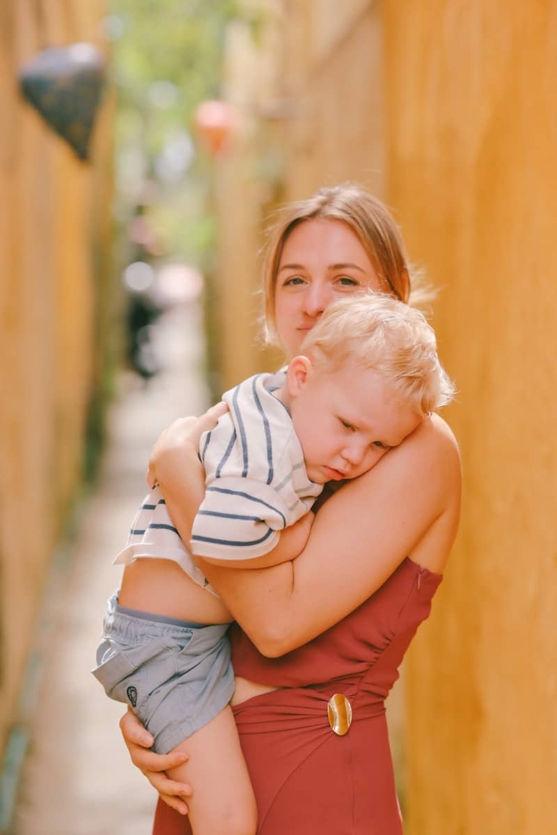 Woman holding a sleeping child in a narrow alley.