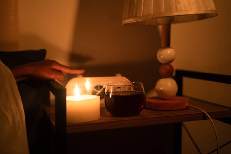 Candle and lamp illuminate a bedside table at night.