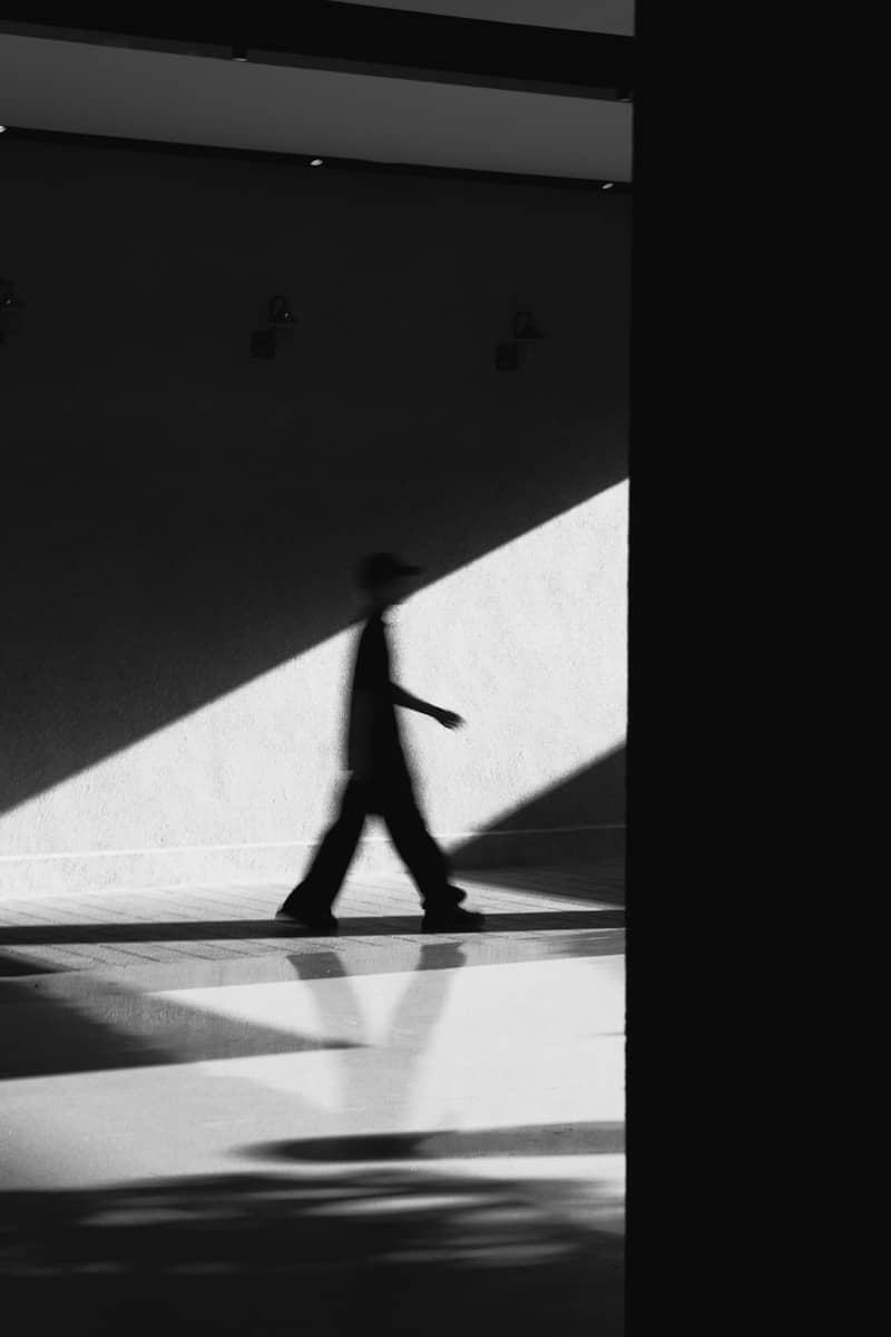 A person's silhouette walks through dramatic light and shadow.