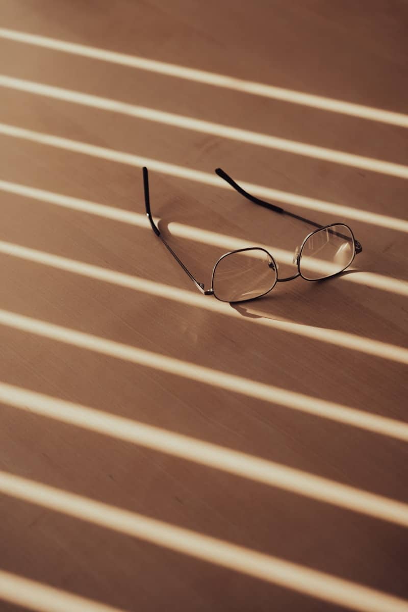 Eyeglasses on a wooden surface with striped shadows.