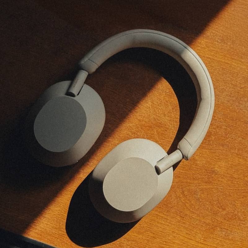 Headphones lay on a wooden surface in sunlight.