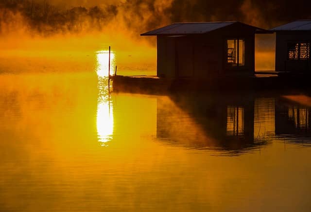 sunrise and fog by boathouse on lake