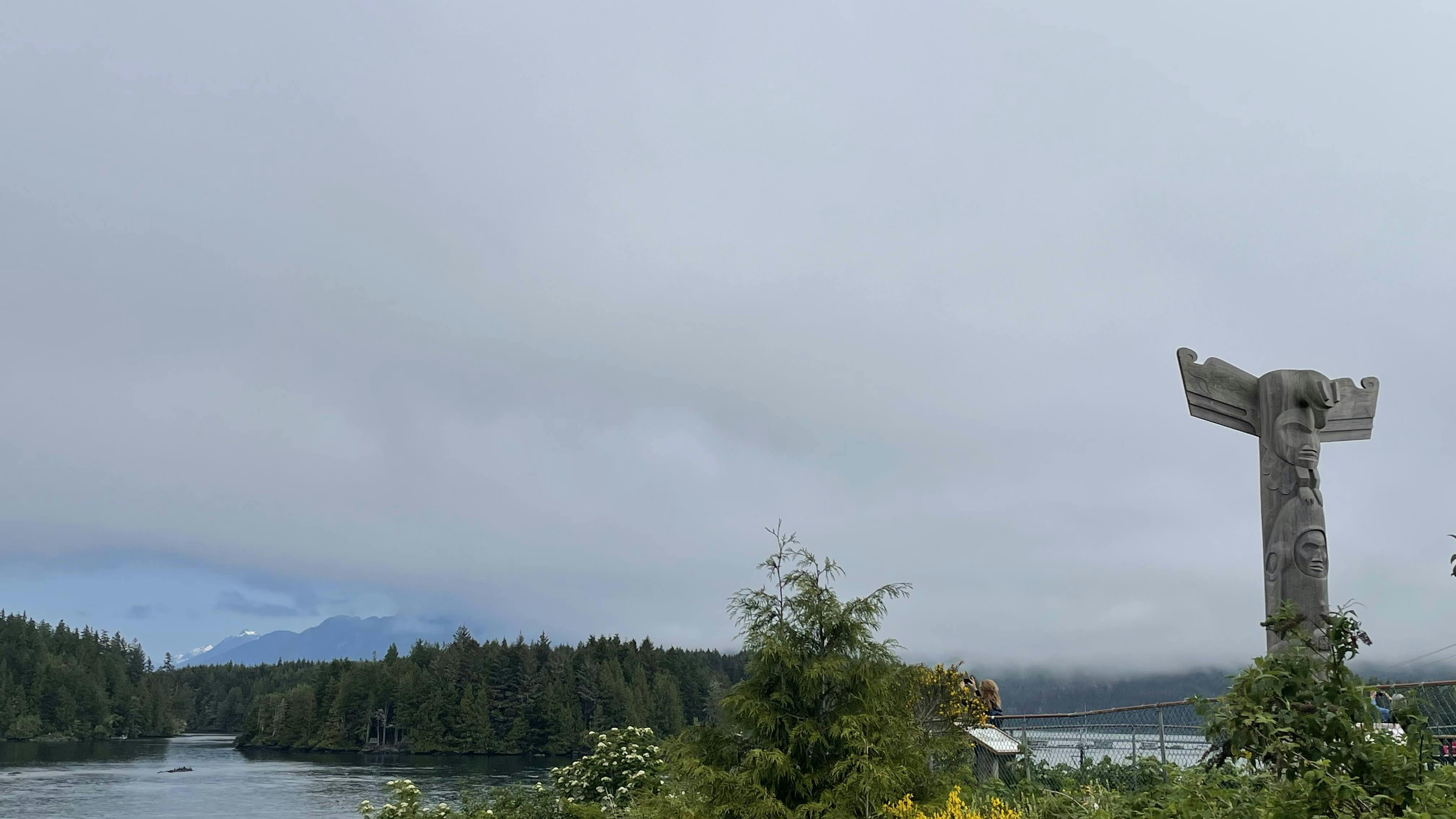 Meare's Island peaking through the clouds. A wooden totem pole off to the side in Tofino, BC.