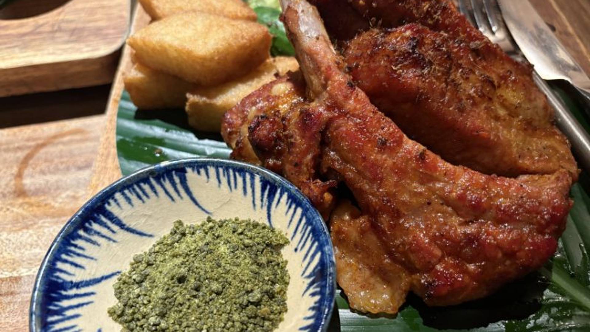 Grilled ribs with crispy skin beside a bowl of green ant salt abnd fried tofu on a banan leaf. 