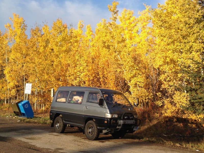 A large van stopped in front of trees with yellow and orange fall foliage