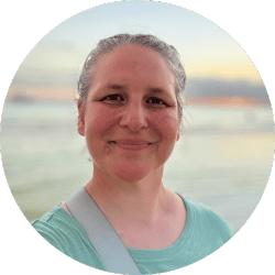 A middle aged smiling woman in front of a beach sunset. 