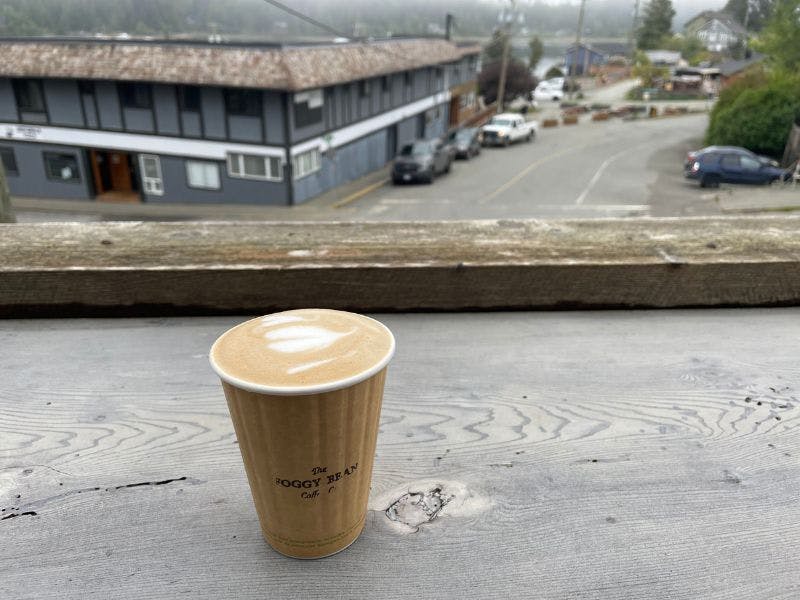 Paper cup of Foggy Bean Cappuccino, with foggy buidligs in background.