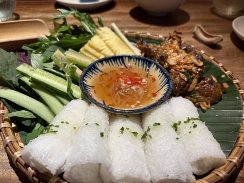 Vietnamese rice rolls, meat, cucumber and pineapple slices on a bamboo serving tray. 