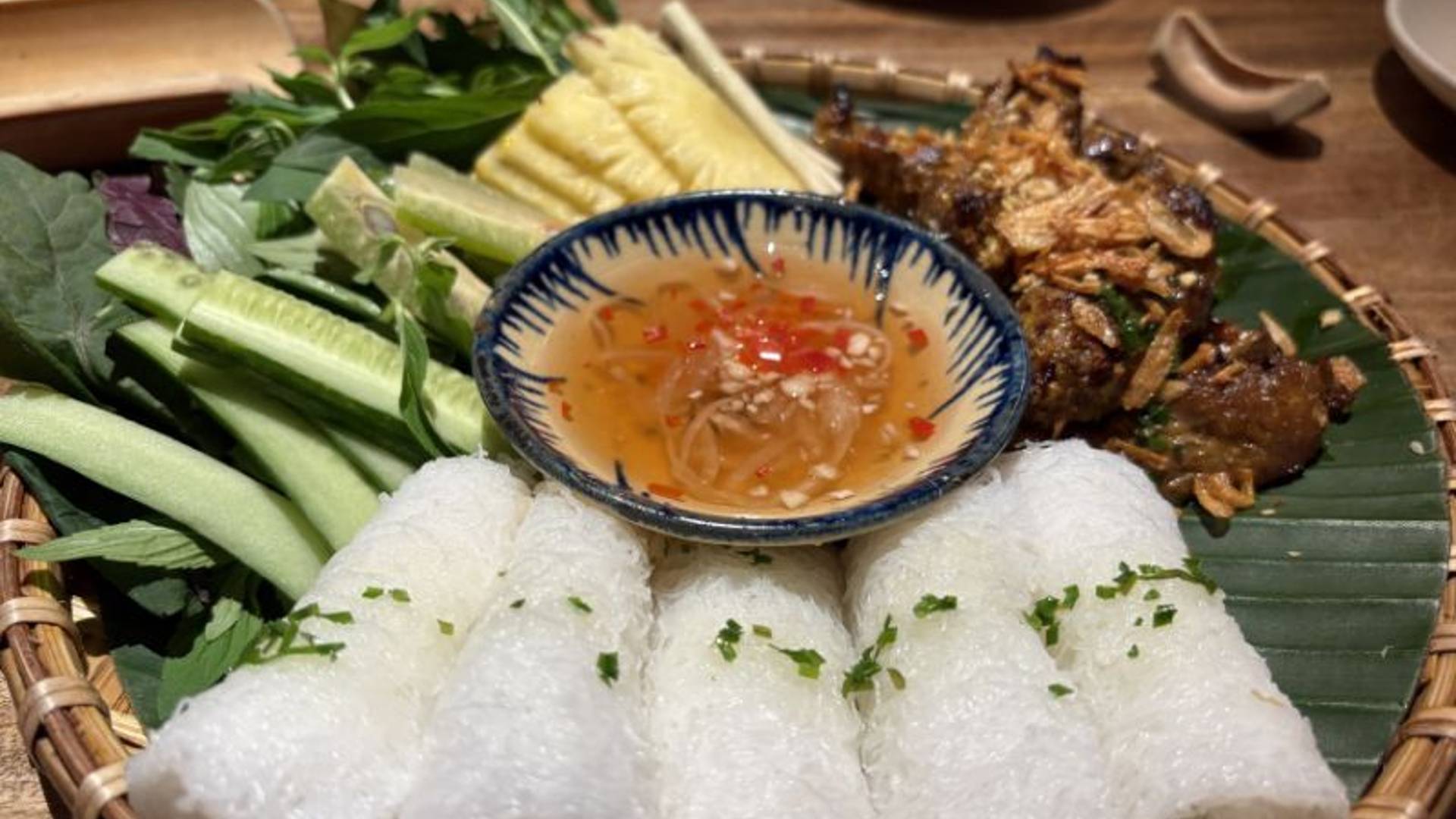 Rice rolls beside nuoc mam dipping sauce, and slices of cucumber, pineapple and beef. 