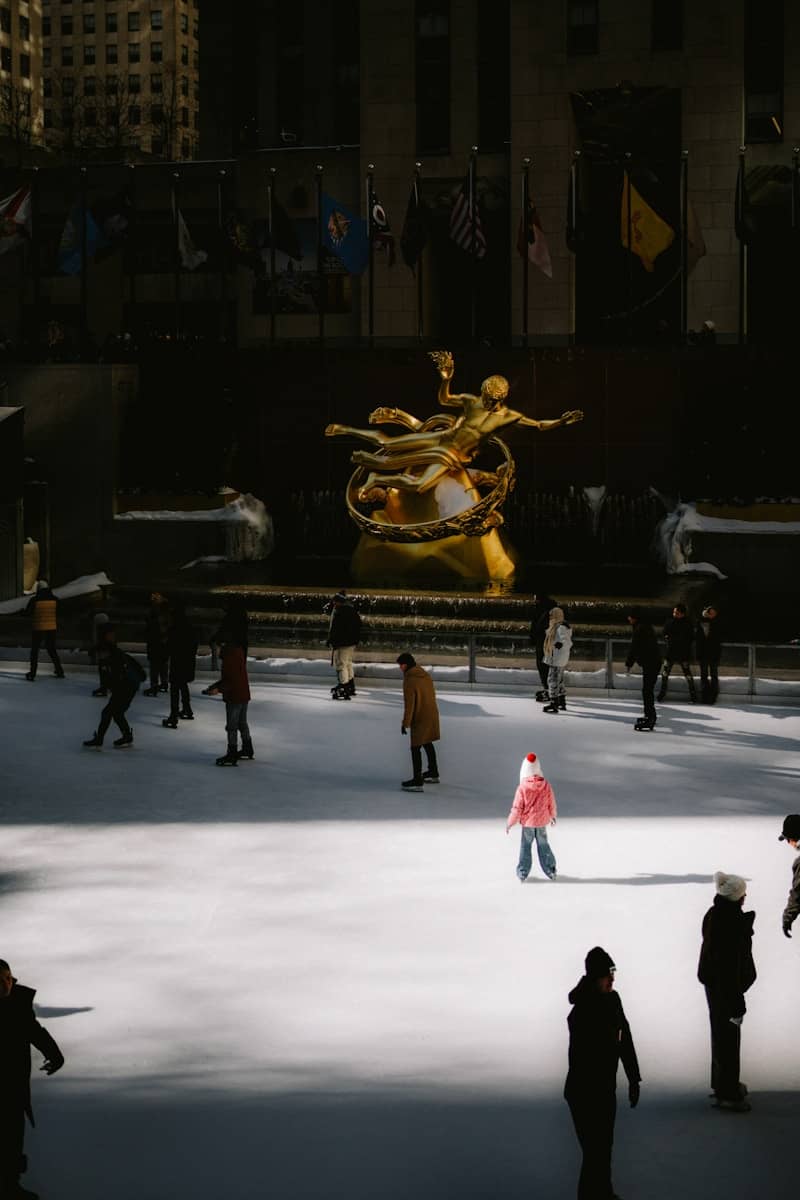 People ice skating in front of a golden statue.