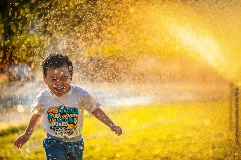 a young boy running through a sprinkle of water