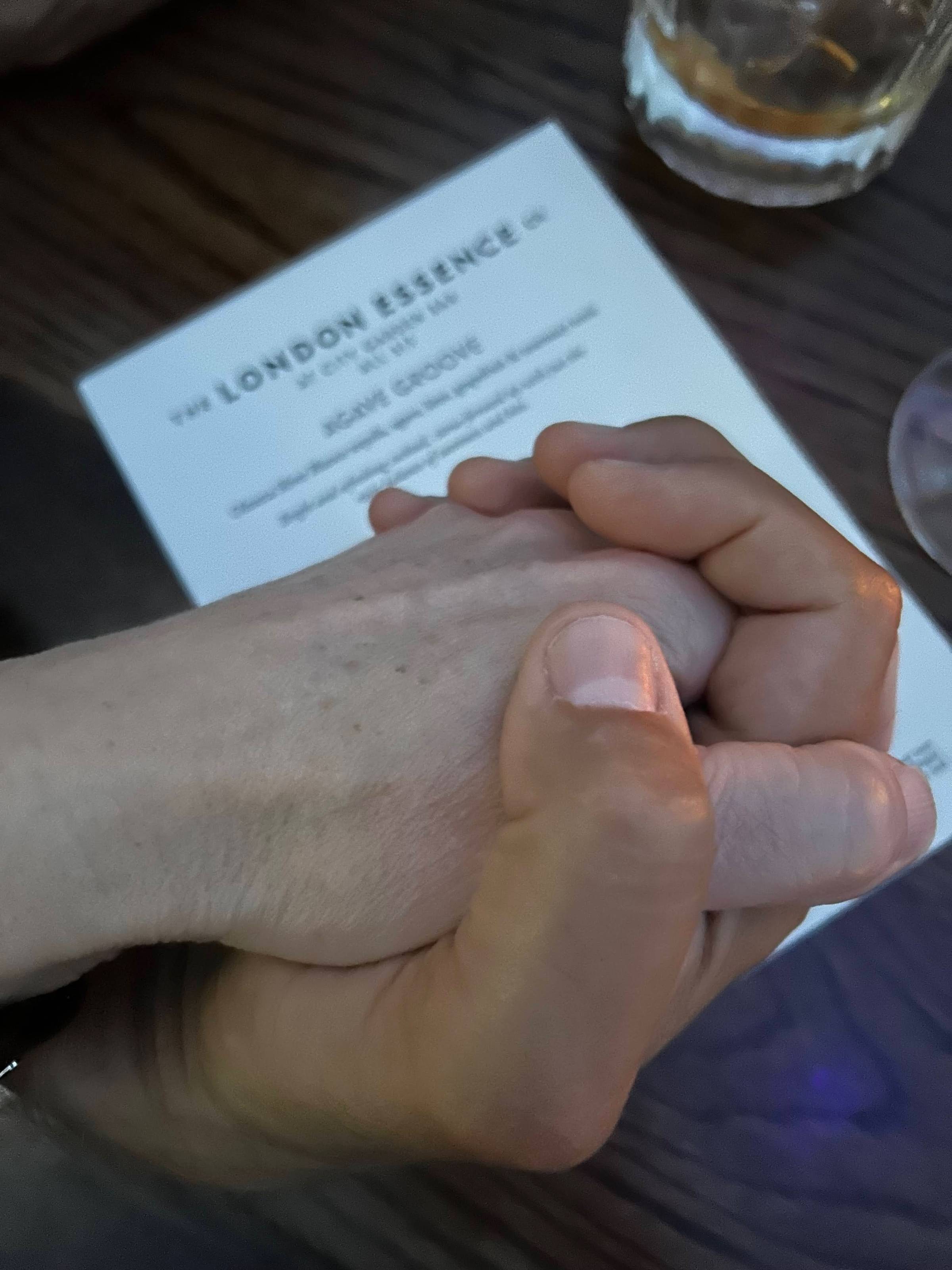 Two hands intertwined on top of a cocktail menu. Mine on top, his on the bottom. Cocktail glasses just barely visible on the right hand edge of the photo