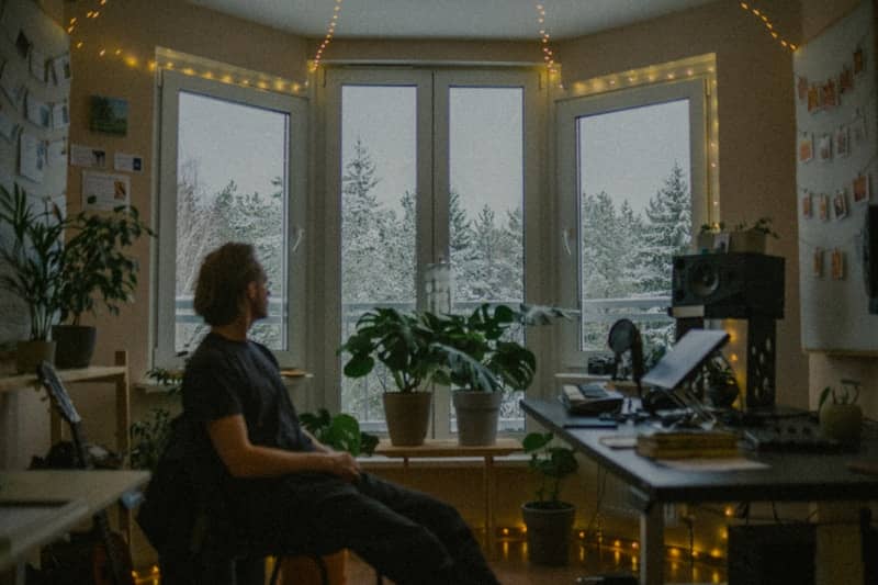 Man looking out window at snowy trees from cozy room.