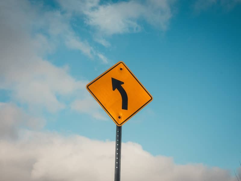 Yellow road sign indicating a sharp left turn.