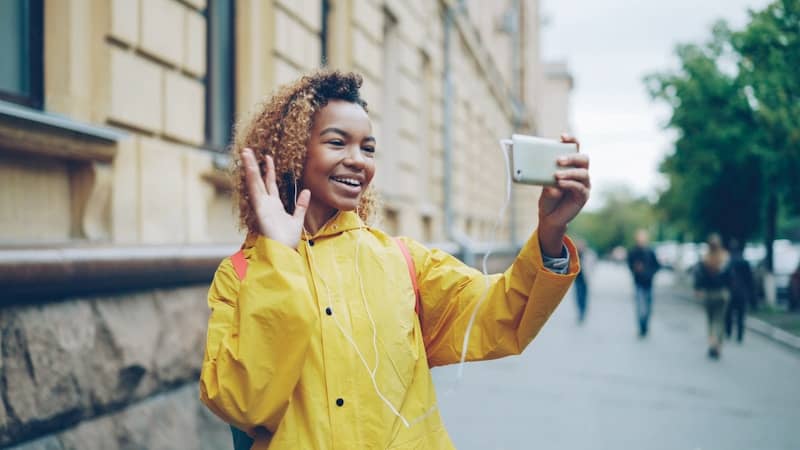 Young woman in yellow coat waves at camera