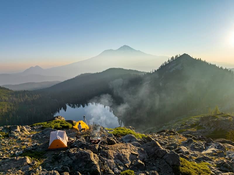 Two tents set up on a rocky cliff overlooking a lake