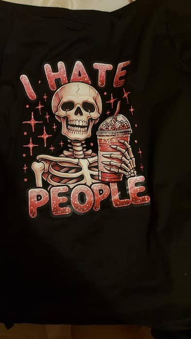 Image of a black t-shirt with I hate people written in pink with a skeleton holding an iced coffee (also pink) in it's hands