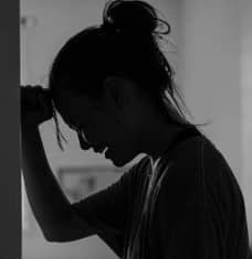A woman leaning against a door, fist supporting her head, crying