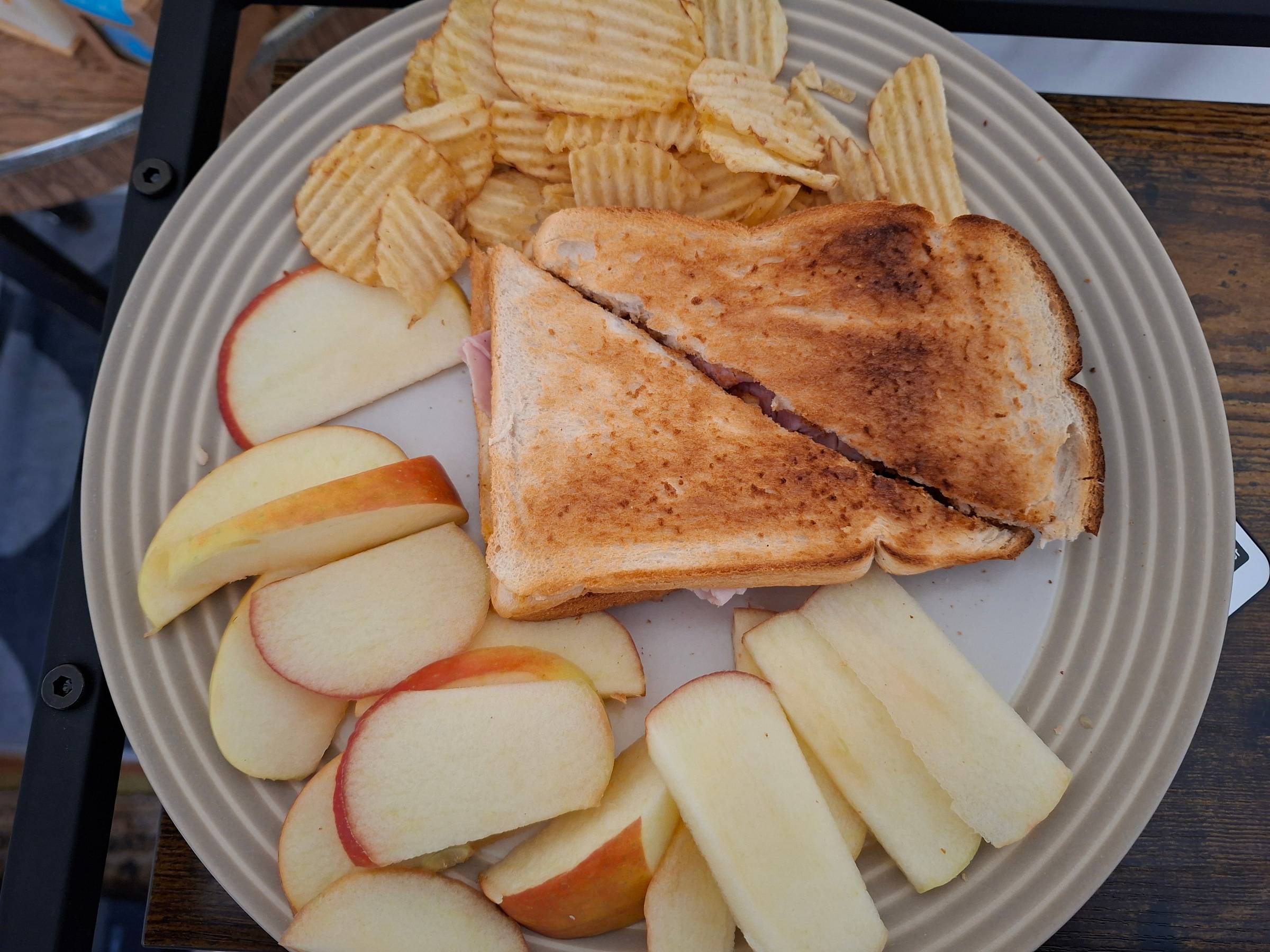 An image of a ham toastie, crisps and a sliced apple