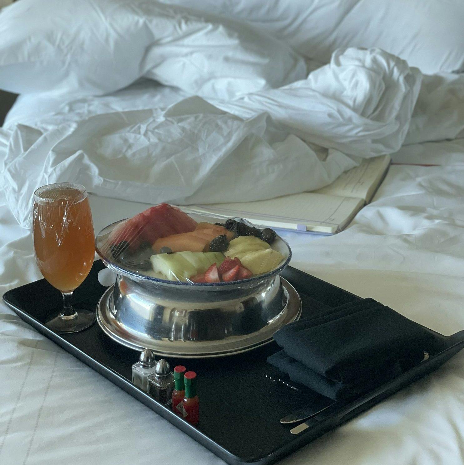 A room service tray with fruit sitting on an unmade hotel room bed