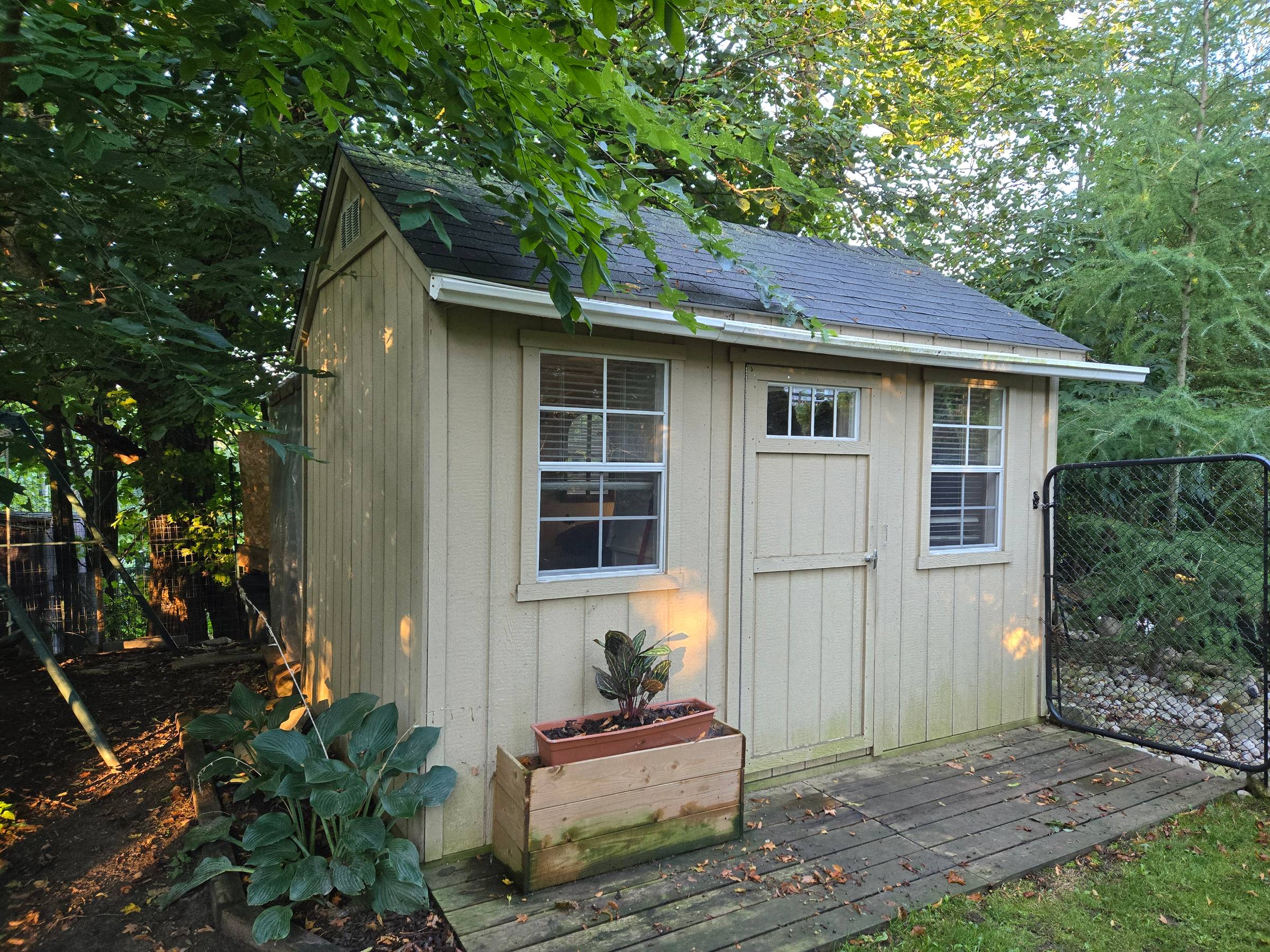 Beige tiny home with windows, door, and plants on a wooden deck.
