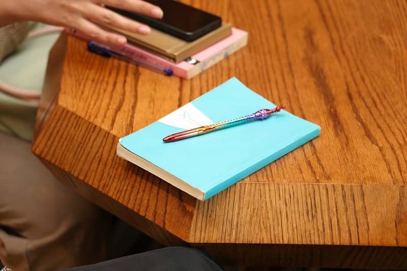 A colorful pen resting on a light blue notebook on a wooden table
