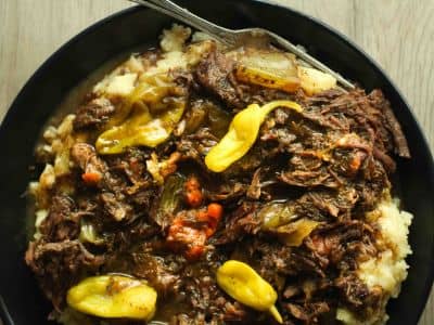 Mississippi pot roast topped with pepperoncini over mashed potatoes in a black bowl.