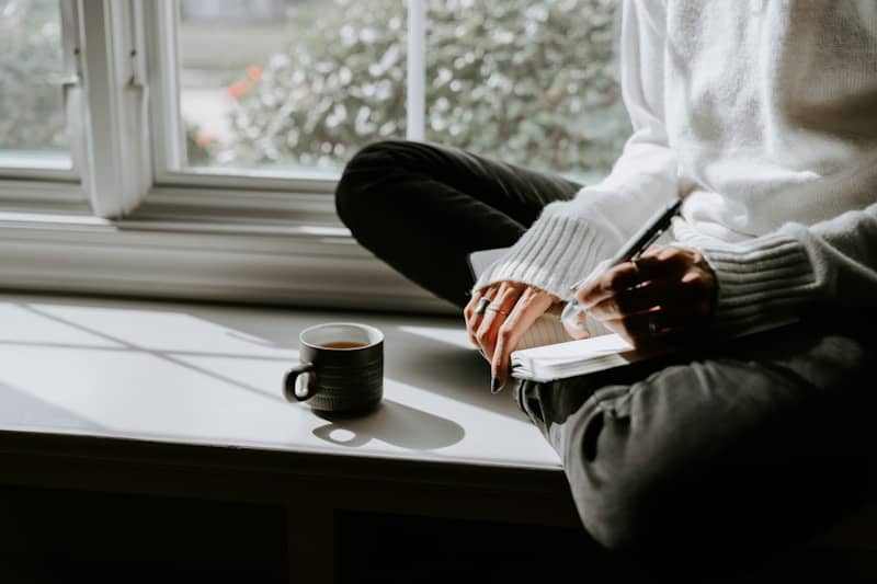 A person sitting on a window sill with a cup of coffee