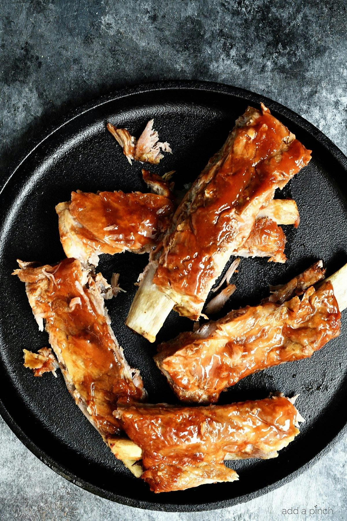 Overhead photograph of ribs on a black plate. 