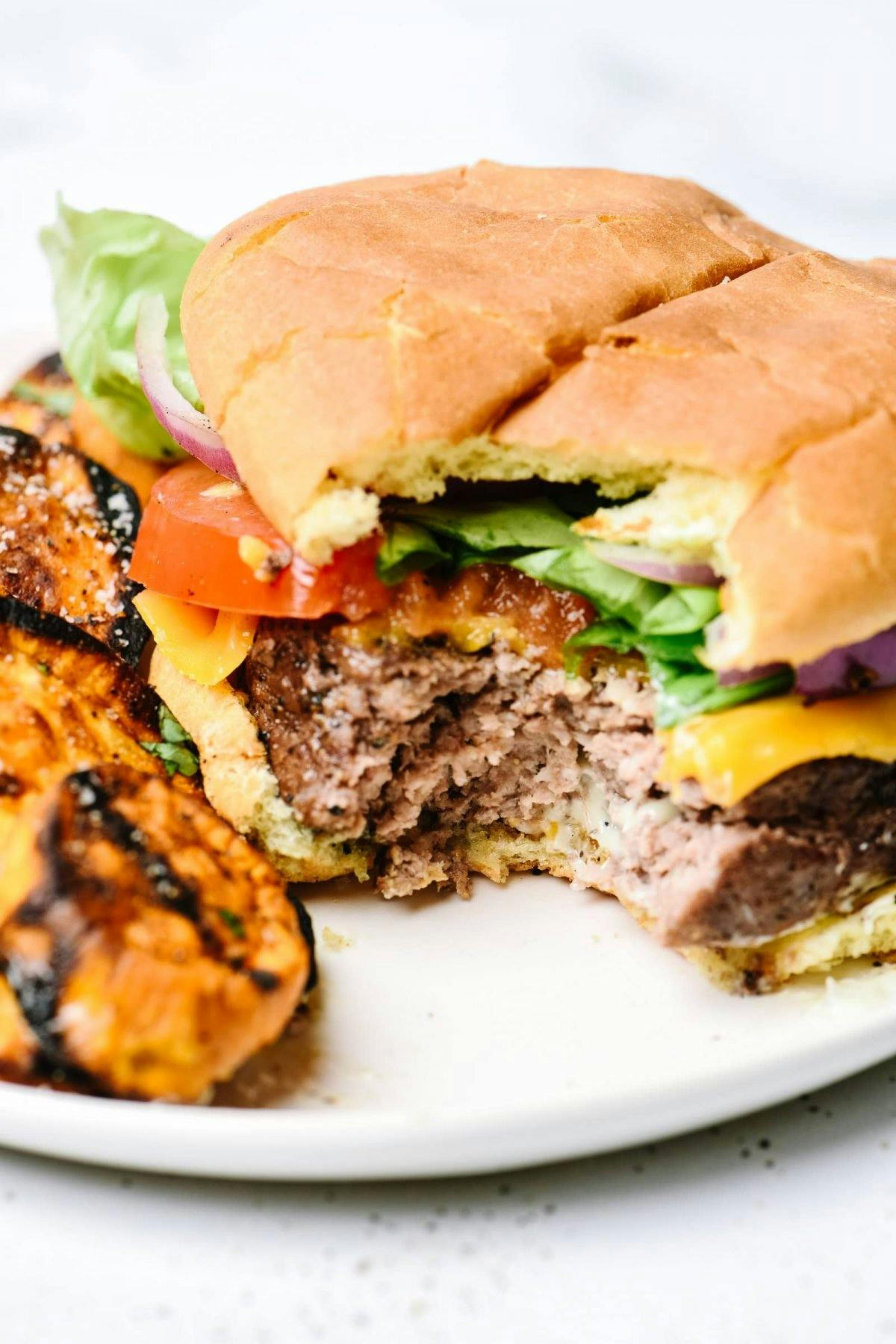 Photograph of hamburger with cheese, lettuce and tomato on a white plate. 