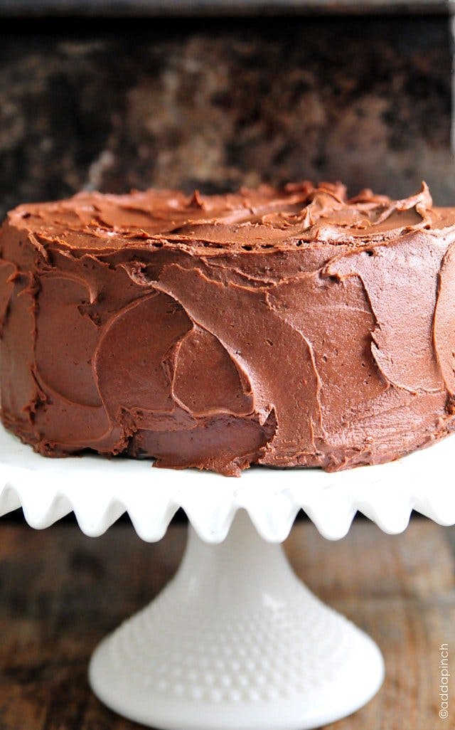 Photograph of chocolate cake with chocolate buttercream frosting on a white cake stand.