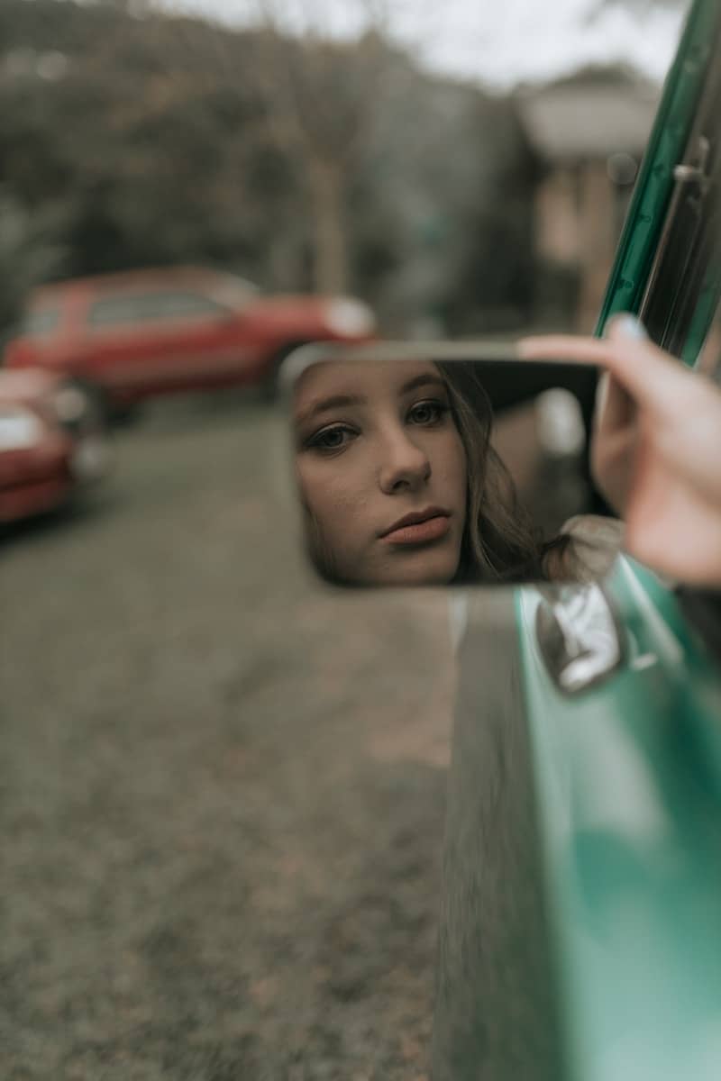 A woman's face reflects in a car's mirror.